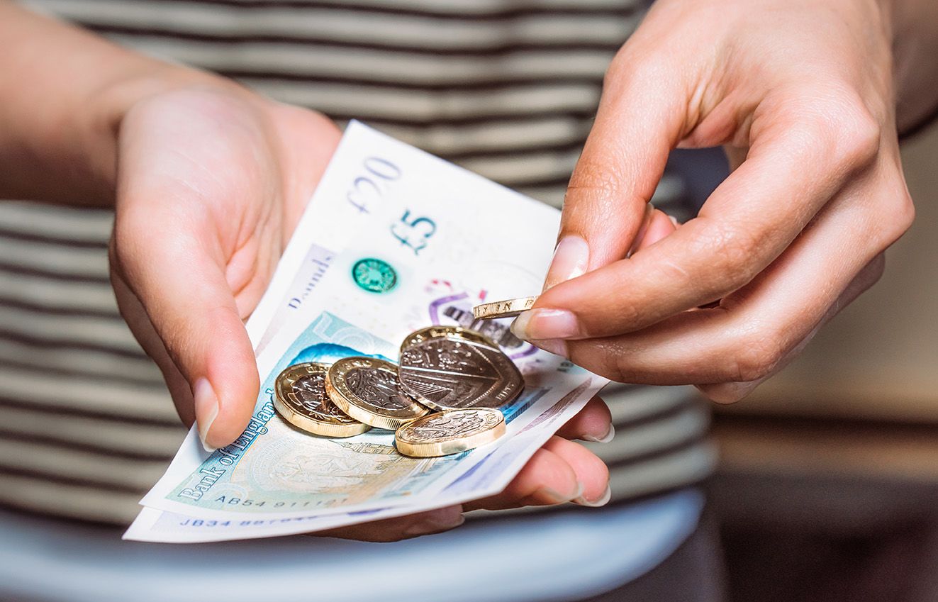A pair of hands holding British pound coins and notes.